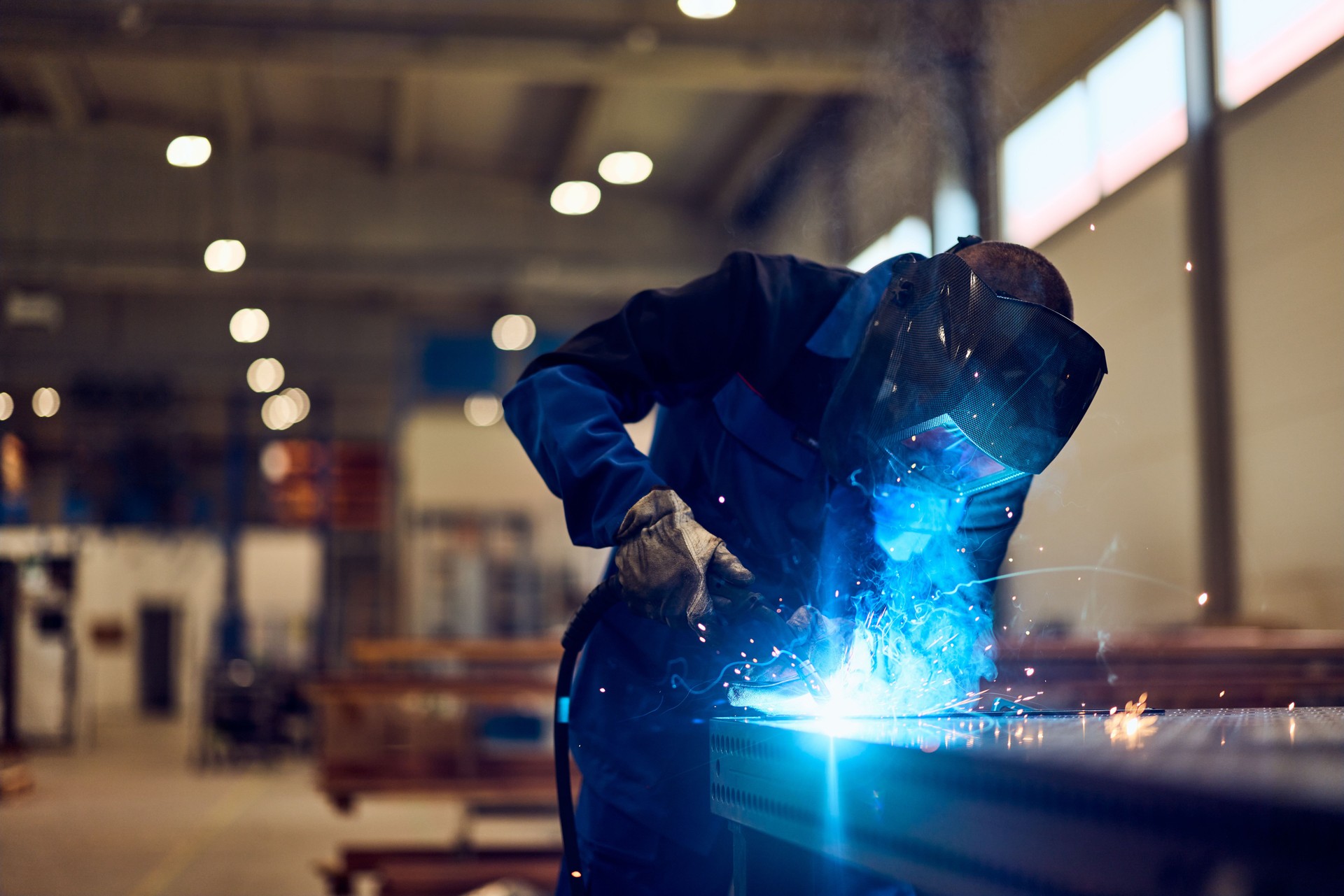 Welder Using Equipment in Industrial Workshop With Blue Welding Sparks